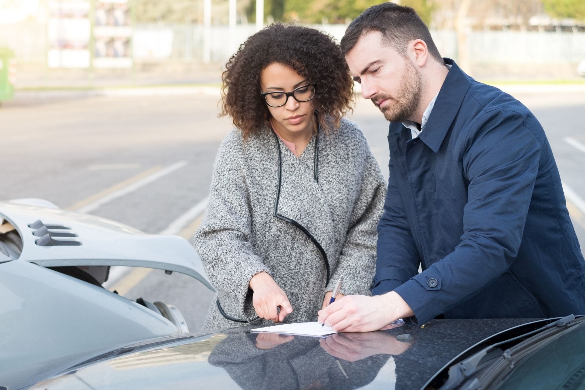 man and woman writing on paper outside on a car