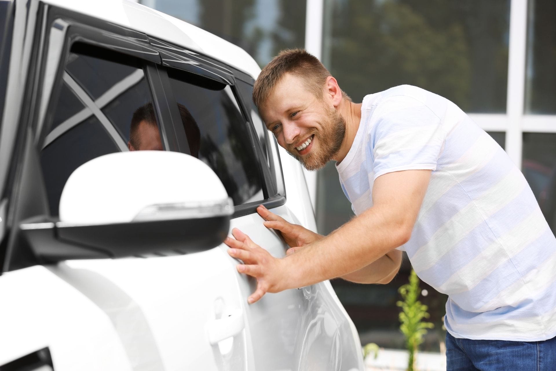 guy wearing white checking on car smiling